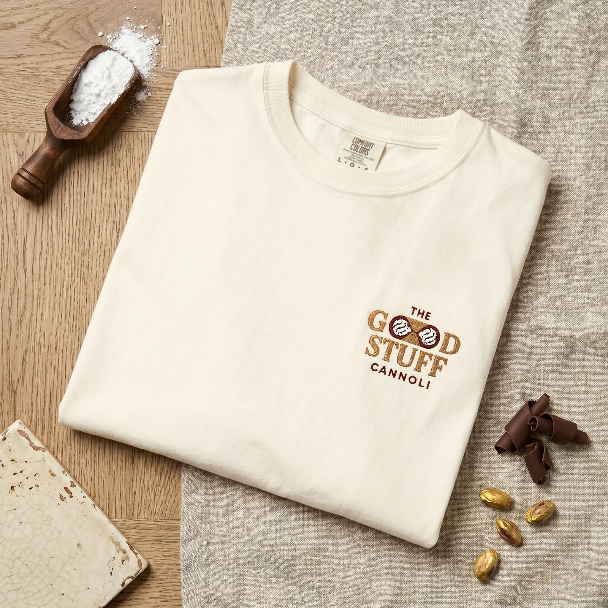 Folded cream t-shirt embroidered with The Good Stuff Cannoli logo